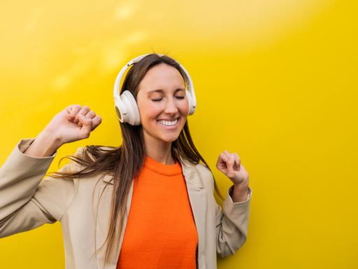 Eine Frau steht tanzend vor einer gelben Wand und tanzt mit geschlossenen Augen