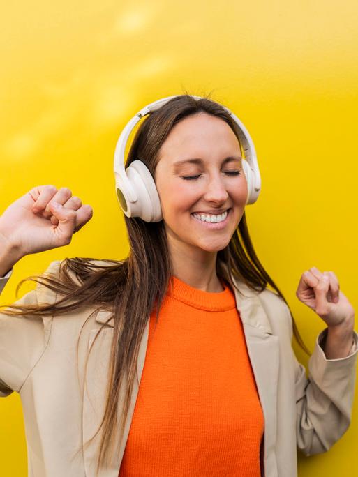 Eine Frau steht tanzend vor einer gelben Wand und tanzt mit geschlossenen Augen
