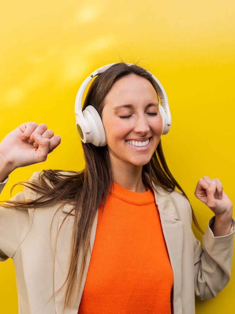 Eine Frau steht tanzend vor einer gelben Wand und tanzt mit geschlossenen Augen