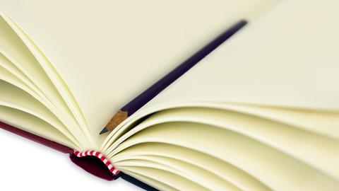 Ein aufgeschlagenes Notizbuch mit leeren Seiten. In der Mitte liegt ein Bleistift.