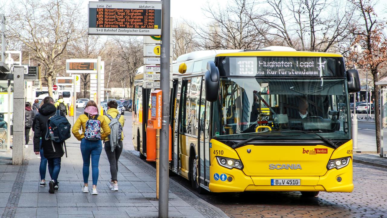 Ein Bus an einer Haltestelle in Berlin. Neben dem Bus läuft eine kleine Gruppe von Jugendlichen über den Bürgersteig. 