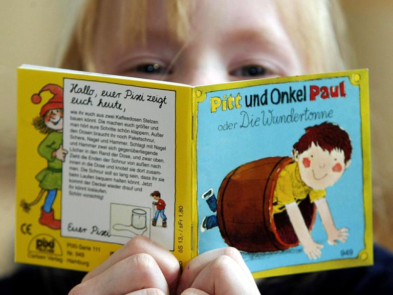 Nahaufnahme eines Kindes, das aus einem kleinen, quadratischen Pixi-Buch liest.