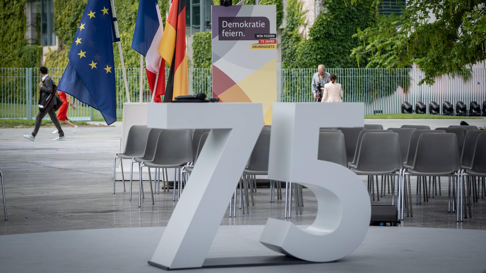 Beim Fest zum Jubiläum des Grundgesetzes steht eine große graue 75 vor einem Plakat "Demokratie feiern".