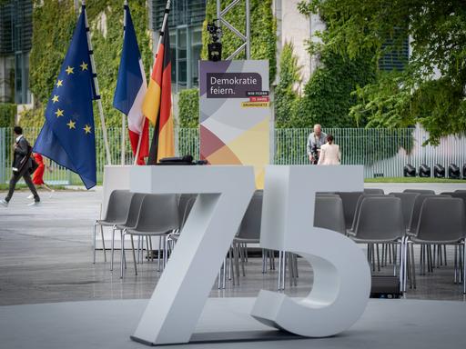 Beim Fest zum Jubiläum des Grundgesetzes steht eine große graue 75 vor einem Plakat "Demokratie feiern".