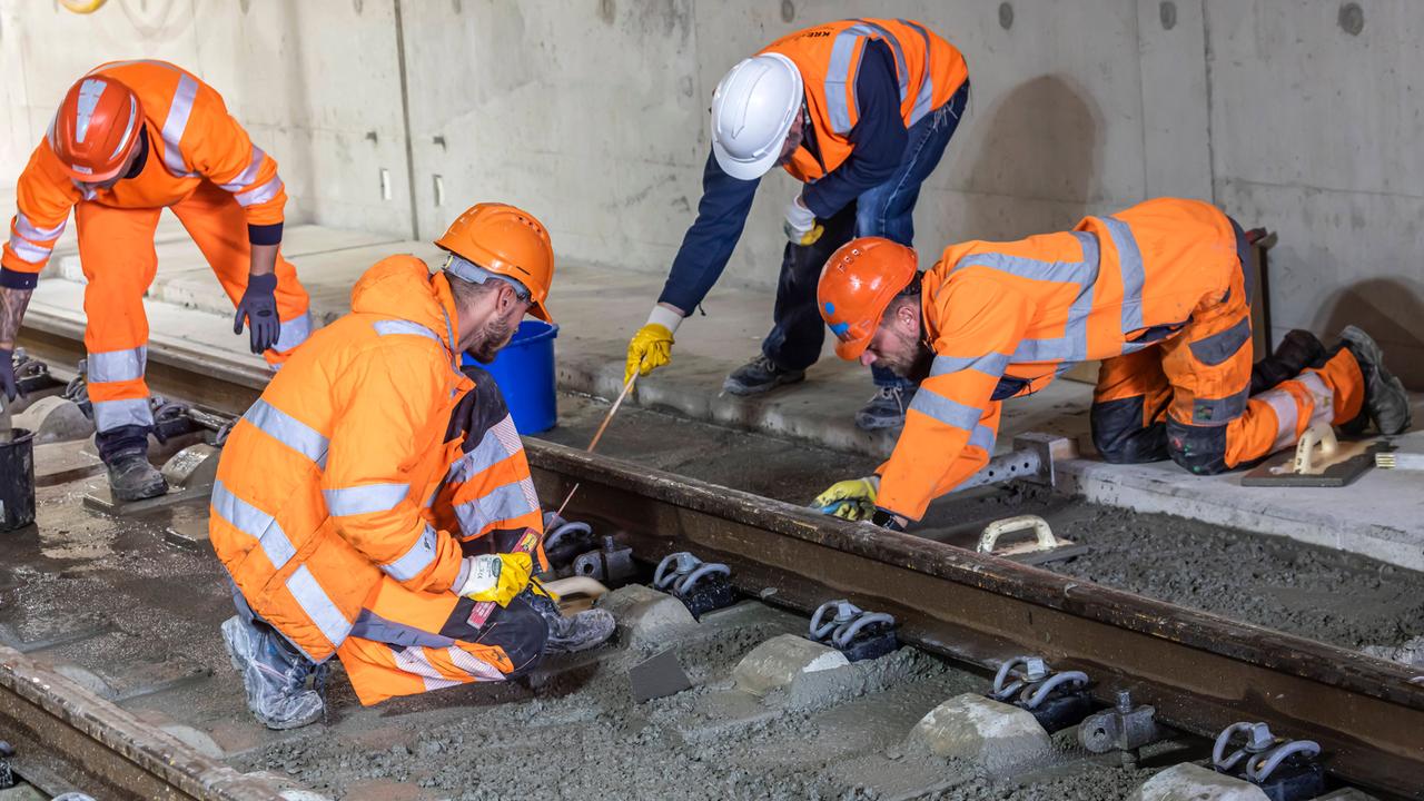Arbeiter in orangen Warnwesten arbeiten gemeinsam an einem Gleisabschnitt.