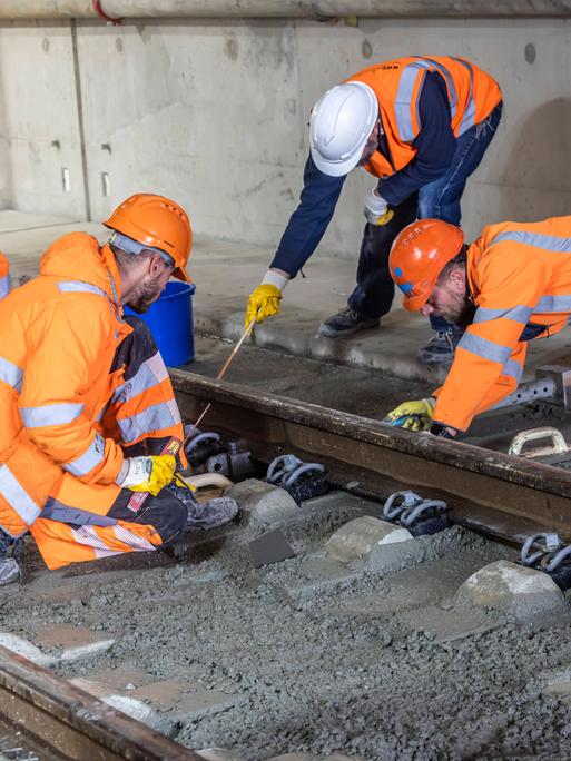 Arbeiter in orangen Warnwesten arbeiten gemeinsam an einem Gleisabschnitt.