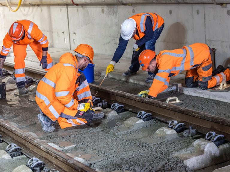 Arbeiter in orangen Warnwesten arbeiten gemeinsam an einem Gleisabschnitt.
