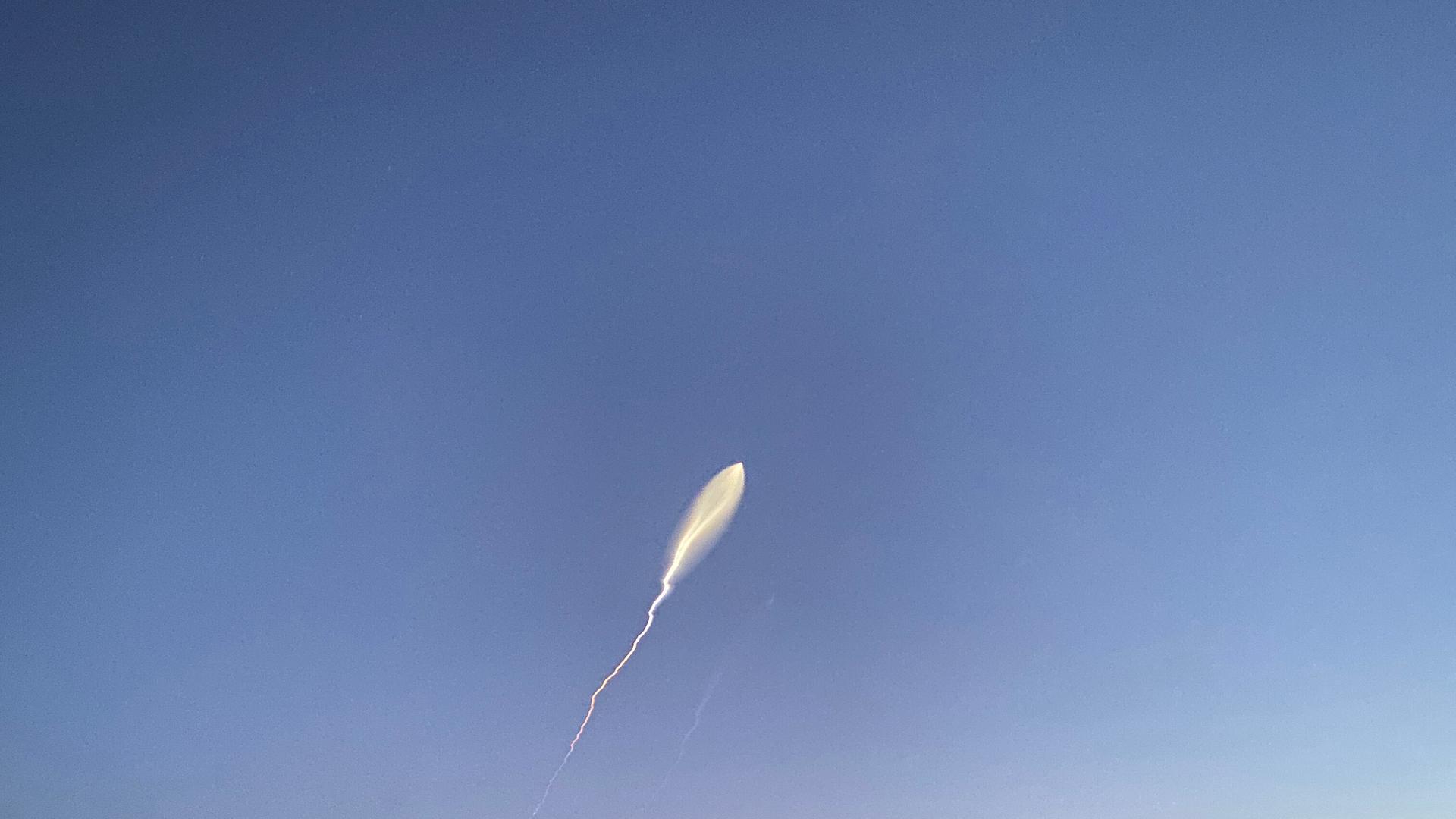 Am blauen Himmel fliegt eine Rakete. Sie hinterlässt einen weißen Schleier.