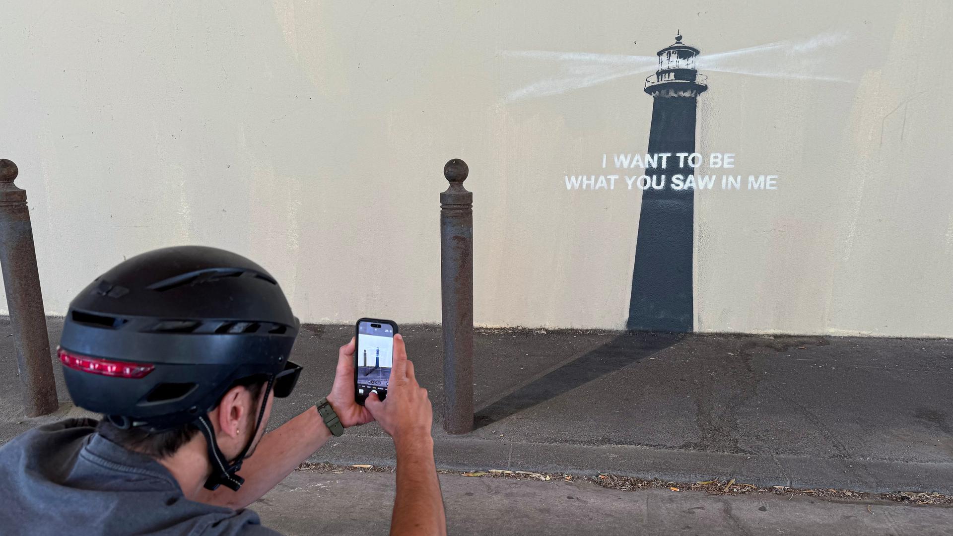 Ein Mann mit Helm fotografiert das neue Kunstwerk von Banksy in Marseille. Es zeigt einen Leuchtturm mit der Botschaft: "Ich möchte sein, was du in mir gesehen hast" Ein Mann mit Helm fotografiert das neue Kunstwerk von Banksy in Marseille. Es zeigt einen Leuchtturm mit der Botschaft: "Ich möchte sein, was du in mir gesehen hast"