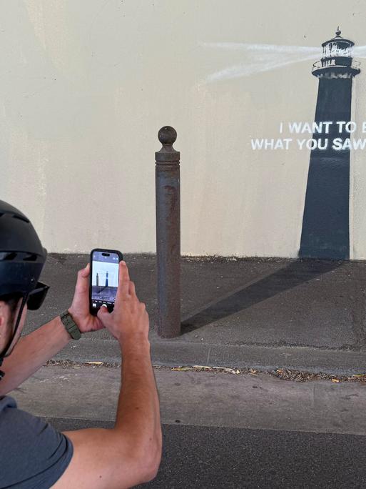 Ein Mann mit Helm fotografiert das neue Kunstwerk von Banksy in Marseille. Es zeigt einen Leuchtturm mit der Botschaft: "Ich möchte sein, was du in mir gesehen hast"