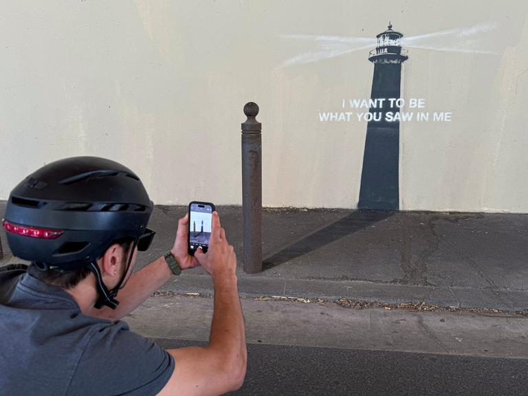 Ein Mann mit Helm fotografiert das neue Kunstwerk von Banksy in Marseille. Es zeigt einen Leuchtturm mit der Botschaft: "Ich möchte sein, was du in mir gesehen hast"
