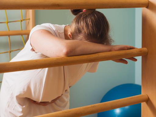 Eine schwangere Frau lehnt in einem Kreißsaal an einer Sprossenwand und stützt den Kopf vor Schmerzen auf den Arm. (Symbolbild) Eine schwangere Frau lehnt in einem Kreißsaal an einer Sprossenwand und stützt den Kopf vor Schmerzen auf den Arm. (Symbolbild)