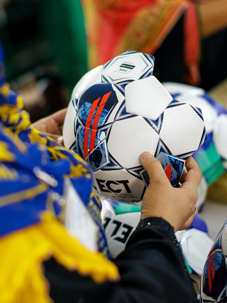Aufnahme einer Person, die einen noch nicht fertiggestellten Fußball in der Hand hält. Die Person trägt ein farbenfrohes Kopftuch und wird von hinten gezeigt. Somit ist ihr Gesicht nicht zu erkennen.
