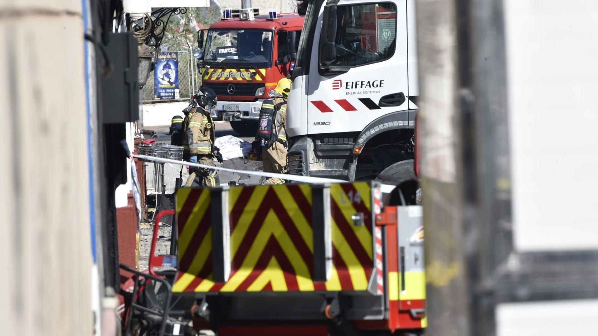 Feuerwehrleute und Einsatzfahrzeuge stehen vor einer Gebäudefassade. Feuerwehrleute und Einsatzfahrzeuge stehen vor einer Gebäudefassade.