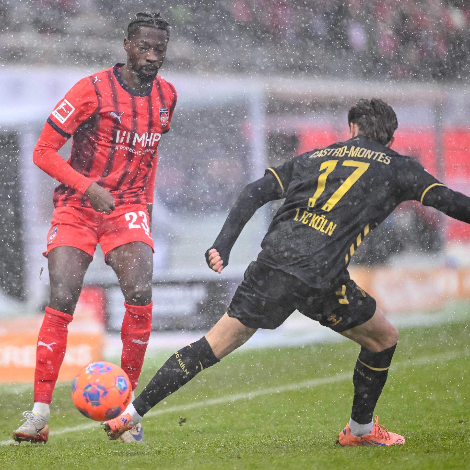 Im dichten Schneetreiben kämpfen beide Spieler um den Ball, der orangefarben ist, um besser erkannt zu werden.