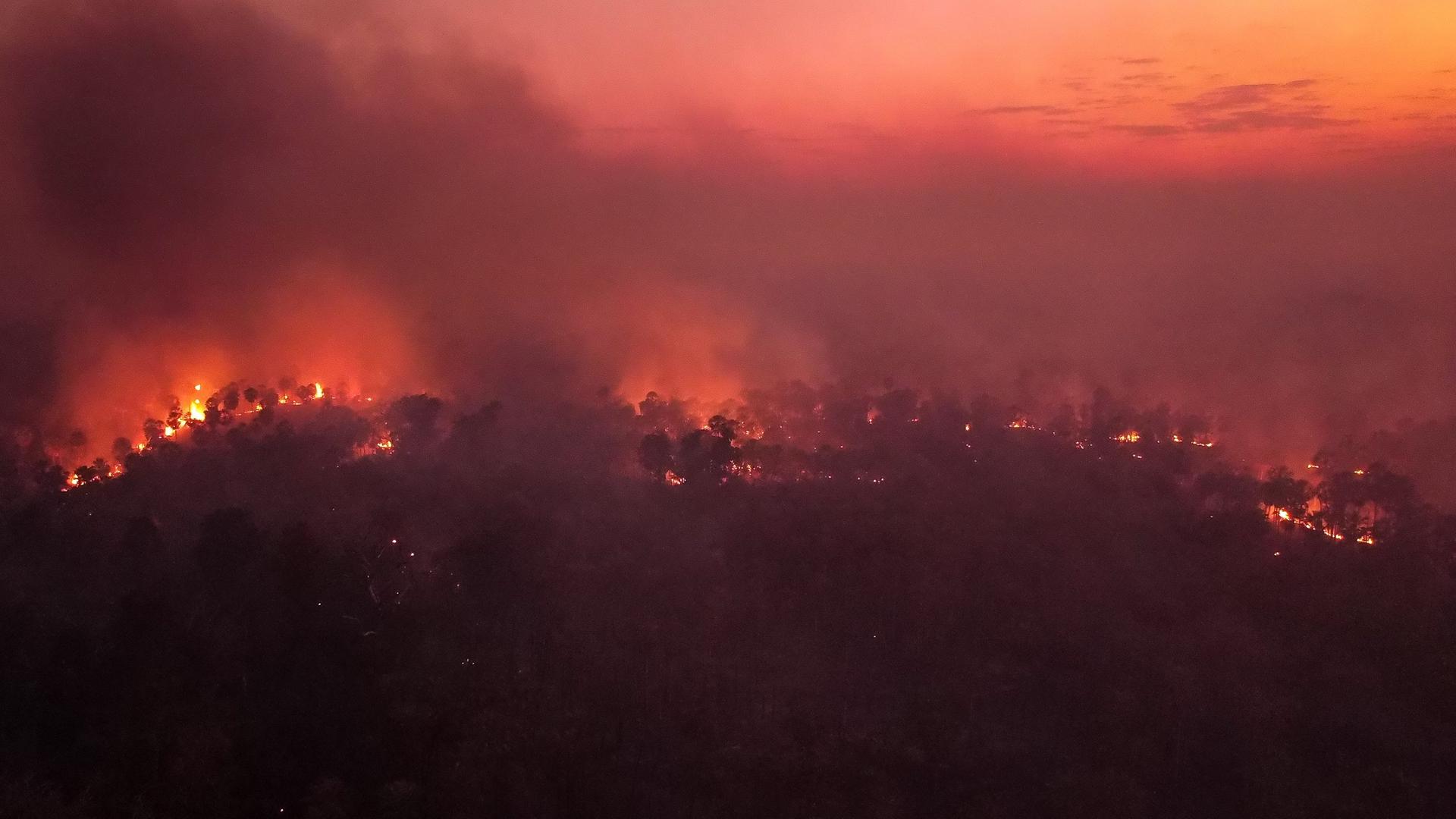 Der Himmel ist rot gefärbt, man sieht viele kleine Feuer und Rauchschwaden.