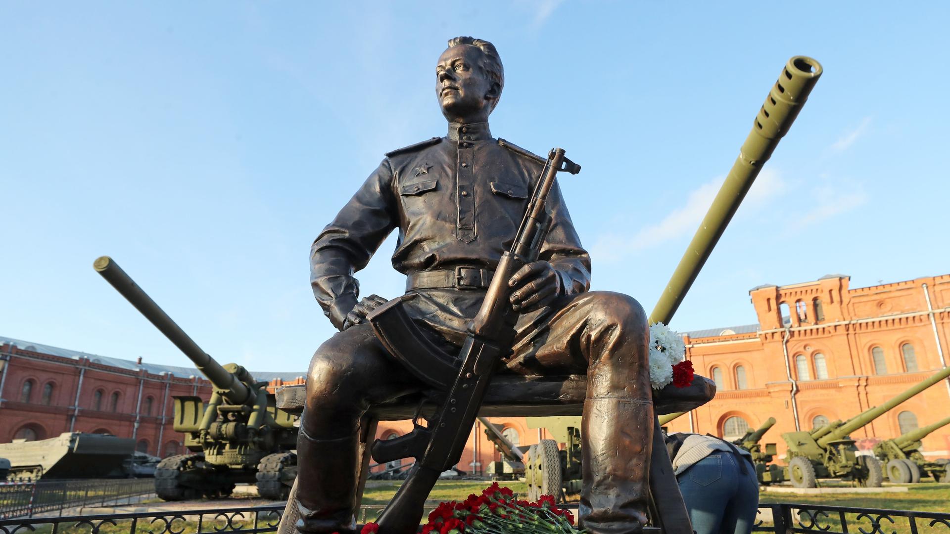 Eine Statue von Michail Kalaschnikow in St. Petersburg, vor der Statue liegen rote Rosen.