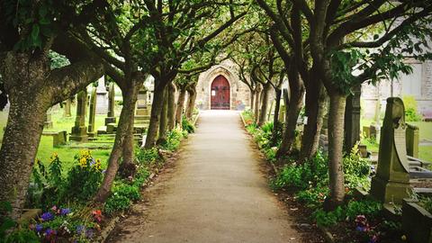 Arbeiten auf einem Friedhof - Einblicke in Abschied und Trauer. Zu sehen: Auf einem Friedhof ein Weg zur Kapelle. 