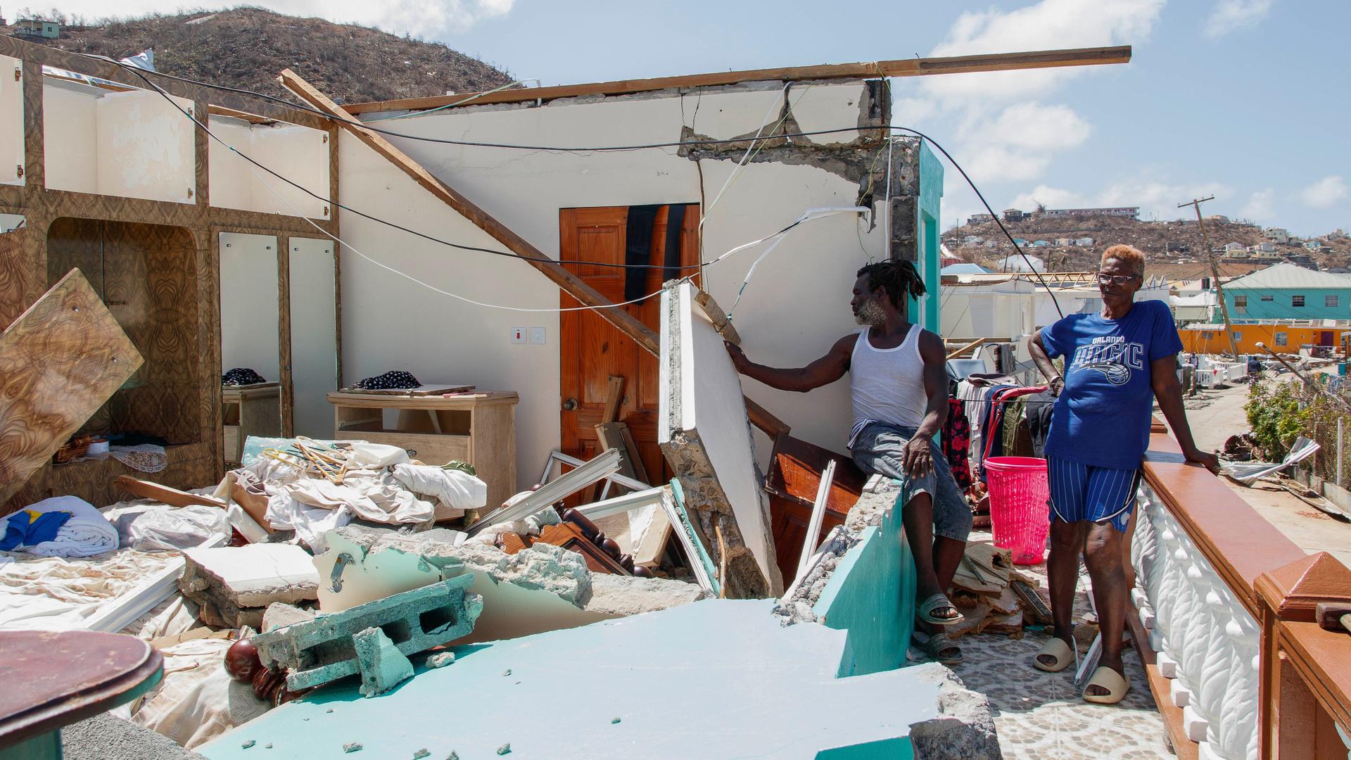 Zwei Menschen stehen neben einem zerstörten Haus. Zwei Menschen stehen neben einem zerstörten Haus.