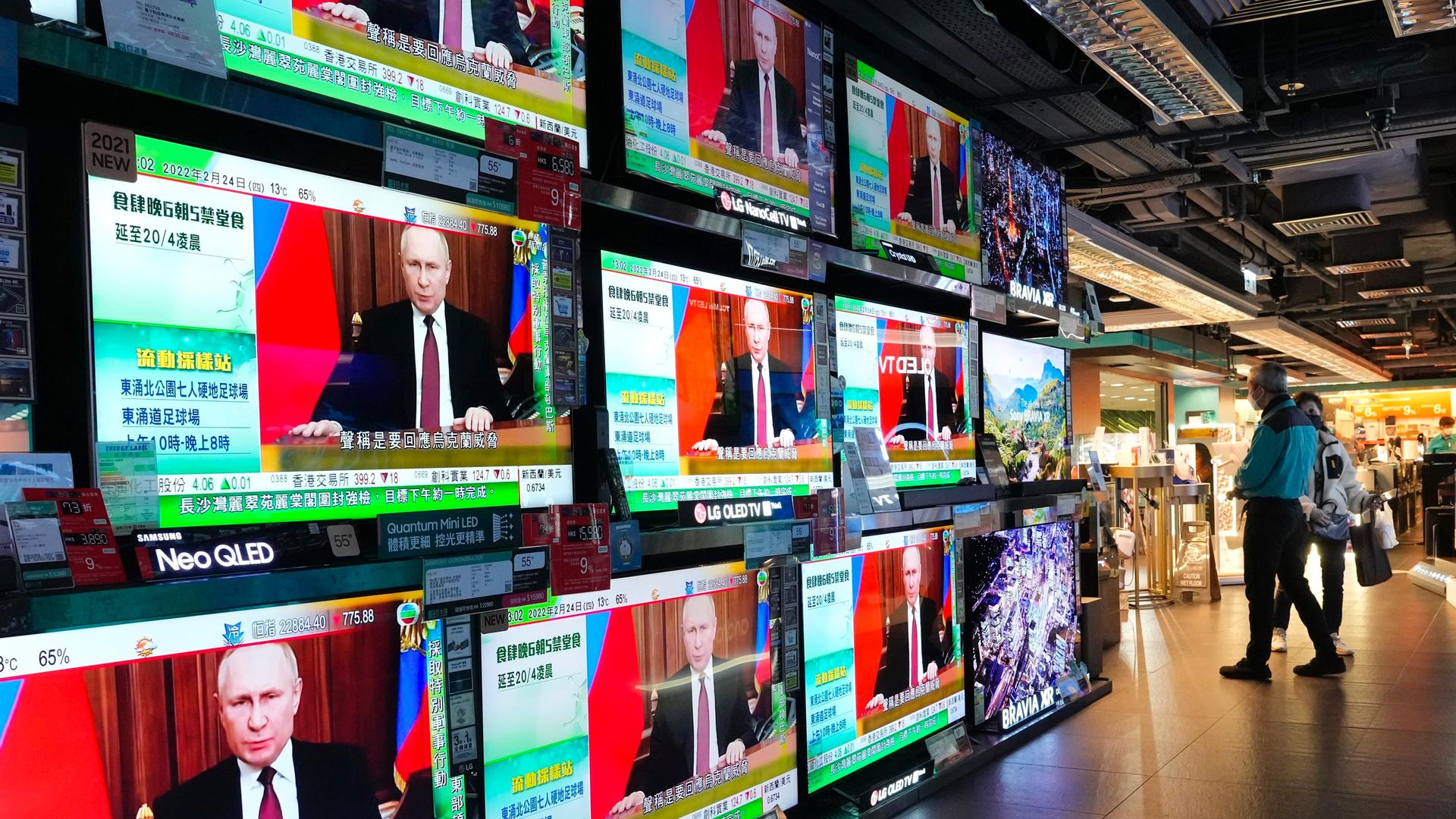 Menschen in Hongkong schauen auf mehrere Fernsehbildschirme, auf denen Putin zu sehen ist.