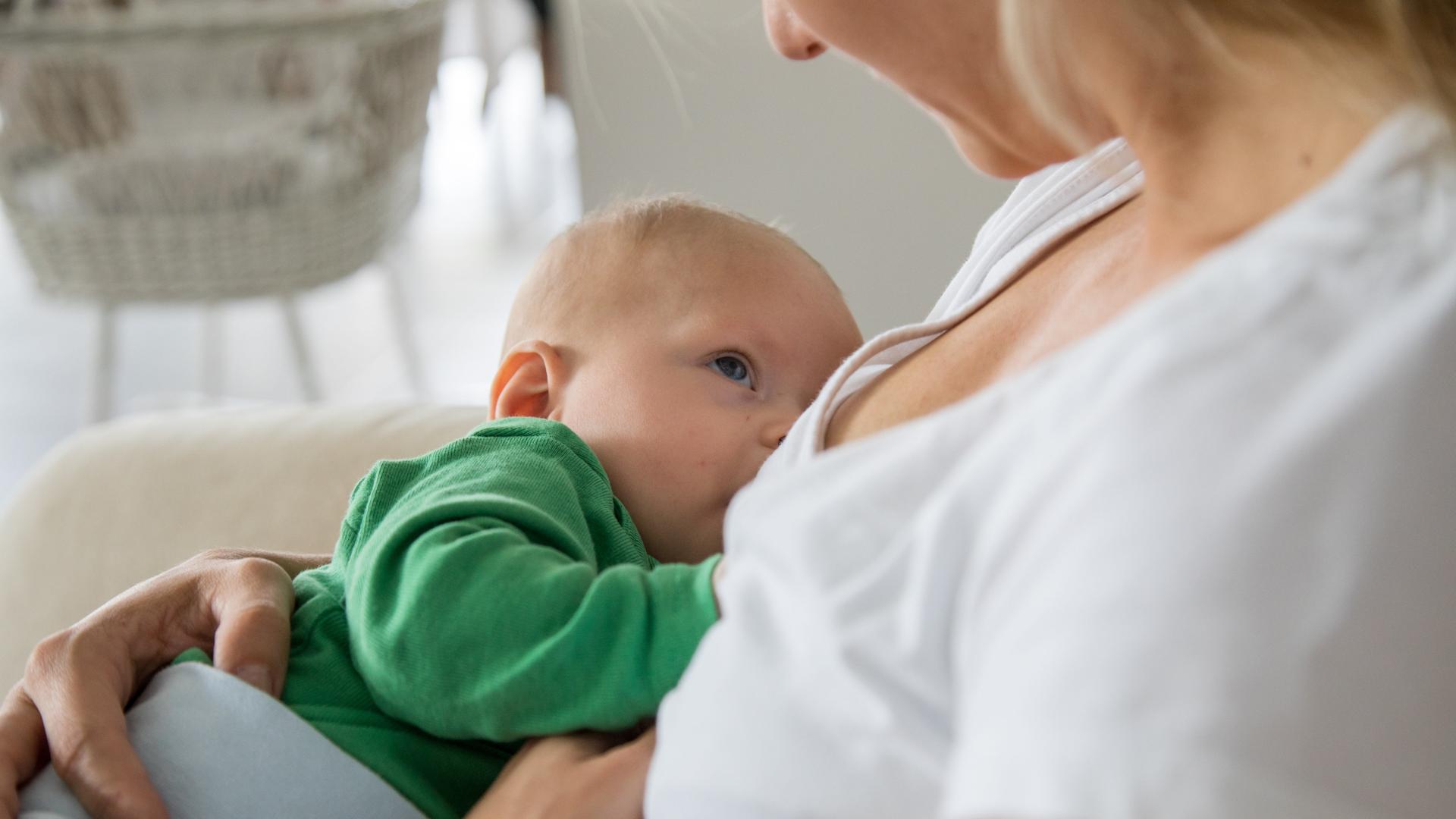 Eine junge Frau haelt ein sechs Monate altes Baby in den Armen und stillt es.