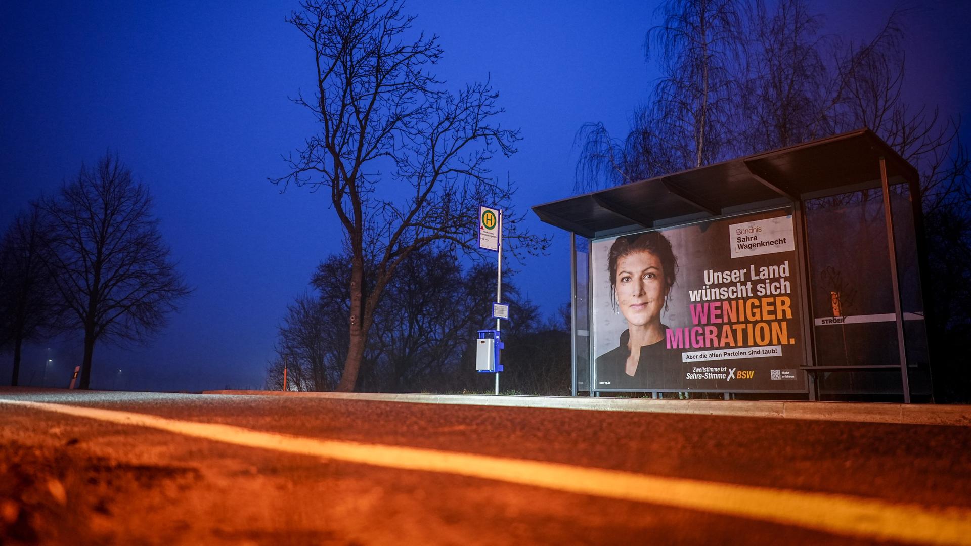 Ein Wahlplakat mit Sahra Wagenknecht, Prarteivorsitzende vom BSW und Bundestagsabgeordnete, ist am frühen Morgen an einer Bushaltestelle zu sehen. Auf dem Plakat ist zu lesen "Unser Land wünscht sich weniger Migration".