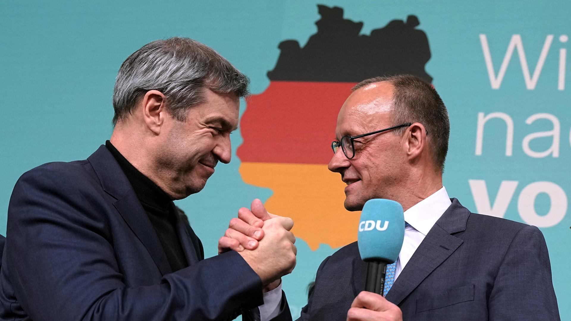 CDU-Chef und Kanzlerkandidat Friedrich Merz gibt CSU-Chef Markus Söder im Konrad-Adenauer-Haus die Hand. Im Hintergrund eine Deutschlandkarte.  