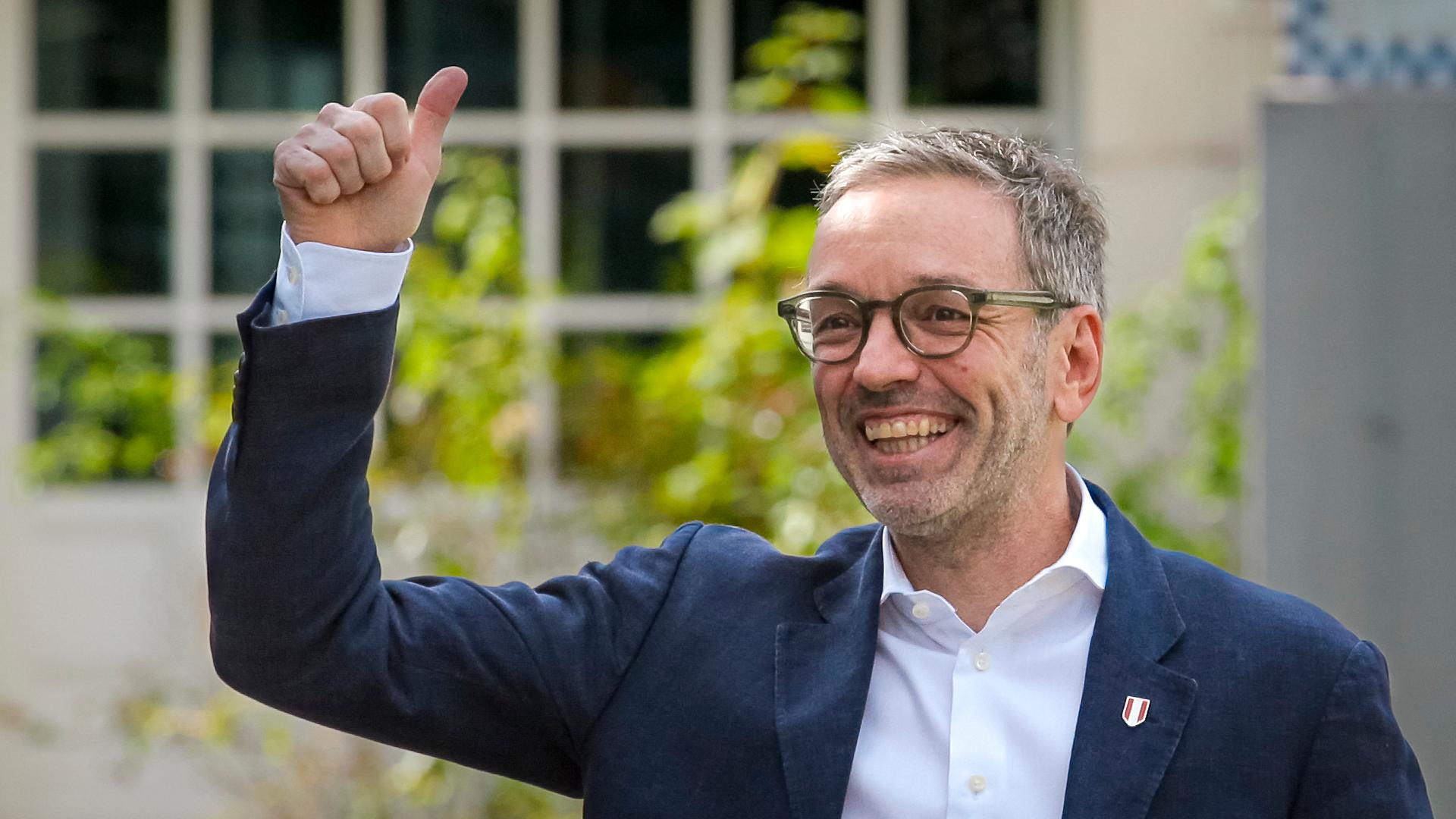 Herbert Kickl - ein grauhaariger Mann mit Brille in einem blauen Anzug. Er hebt den Daumen und lacht.