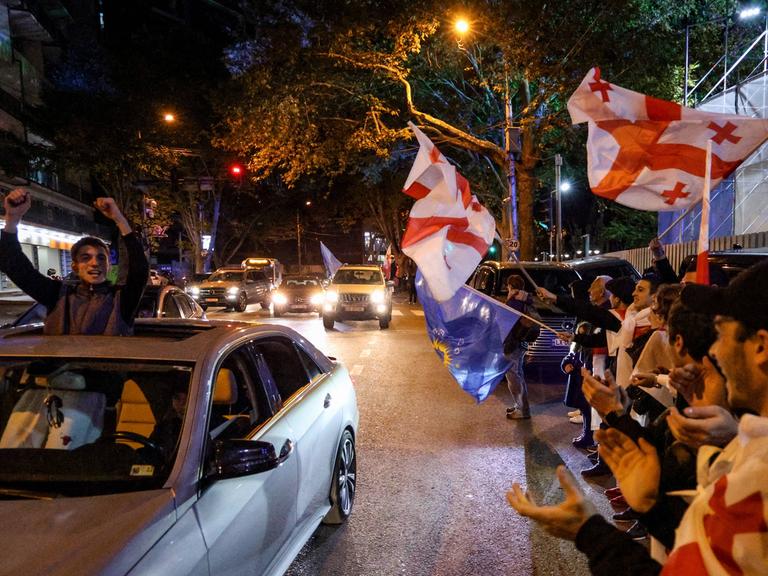 Menschen mit georgischen Flaggen stehen in Tiflis am Straßenrand und feiern den Wahlerfolg der Partei "Georgischer Traum"