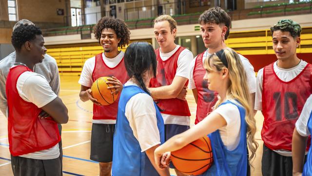 Junge Männer und Frauen stehen beim Basketball-Training nebeneinander.