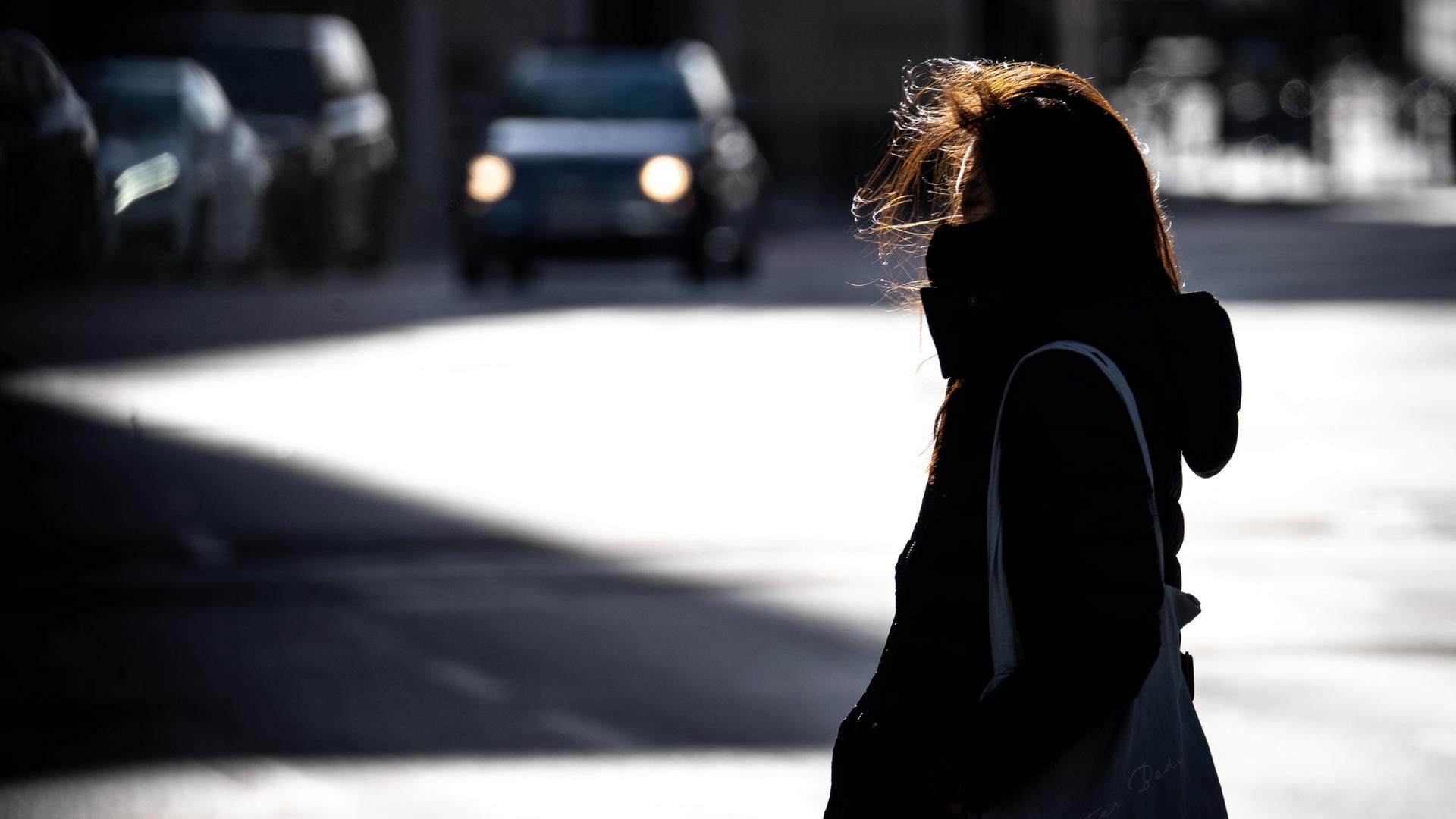 Eine Frau überquert bei windigem Wetter eine Straße in der Frankfurter Innenstadt. Sie wirkt allein und einsam.