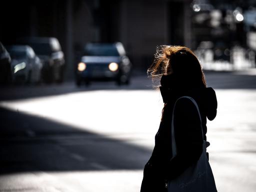 Eine Frau überquert bei windigem Wetter eine Straße in der Frankfurter Innenstadt. Sie wirkt allein und einsam.