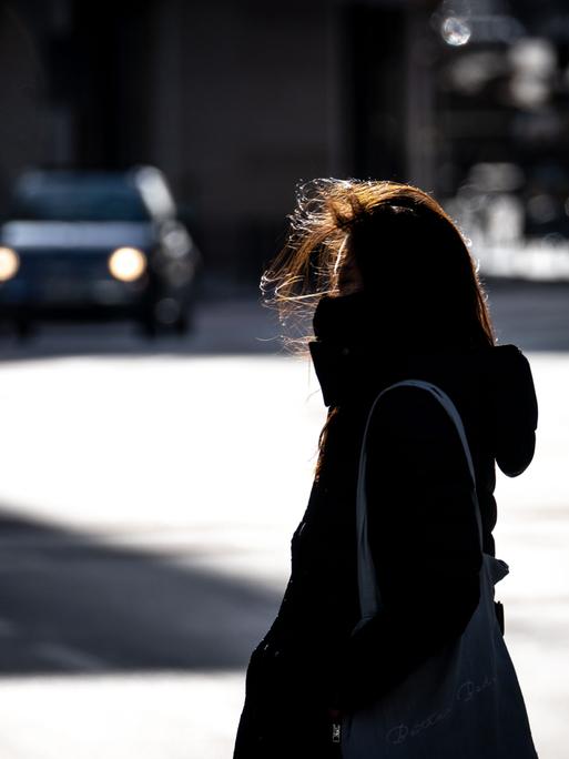 Eine Frau überquert bei windigem Wetter eine Straße in der Frankfurter Innenstadt. Sie wirkt allein und einsam.