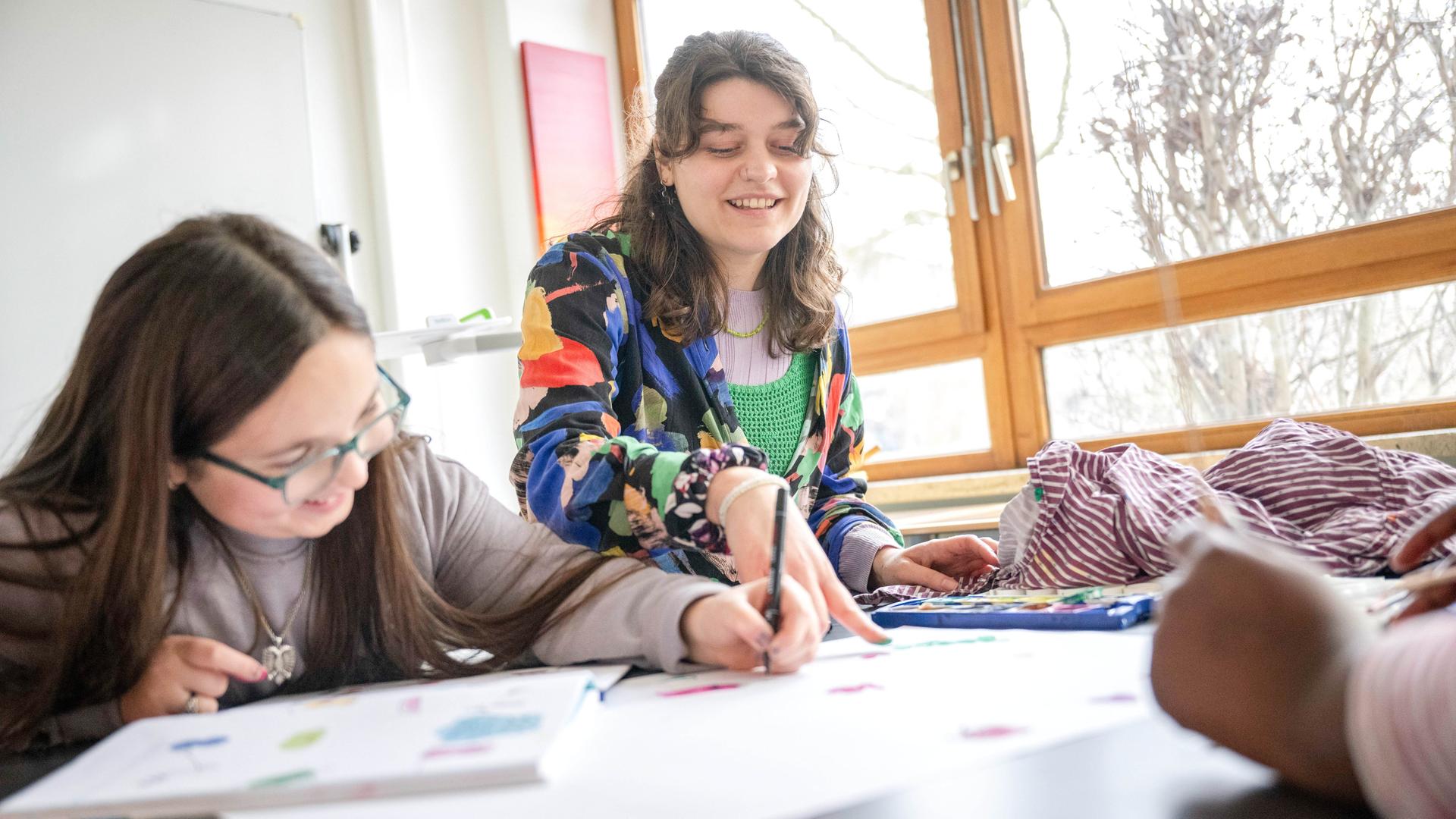 Eine junge Frau gibt in einem hellen Klassenzimmer Nachhilfeunterricht.