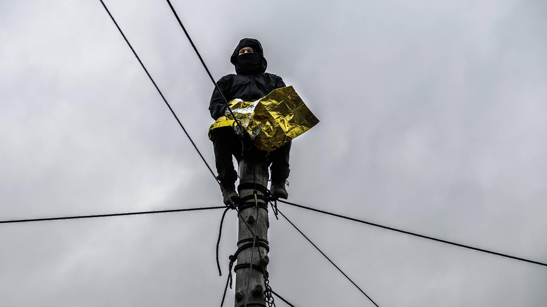 Ein Klimakativist sitzt in Lützerath auf einem Pfahl, gesichert mit Seilen