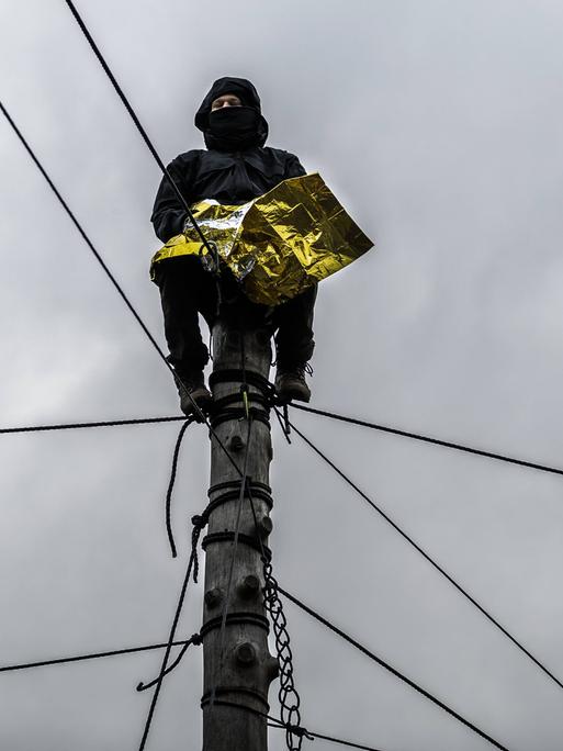Ein Klimakativist sitzt in Lützerath auf einem Pfahl, gesichert mit Seilen