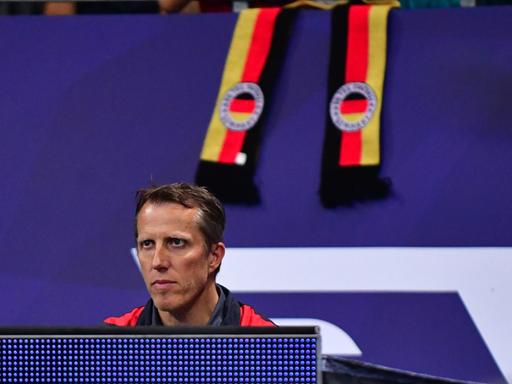 Tischtennis-Herren-Bundestrainer Jörg Rosskopf sitzt hinter einer blauen Bande und beobachtet das Spielgeschehen