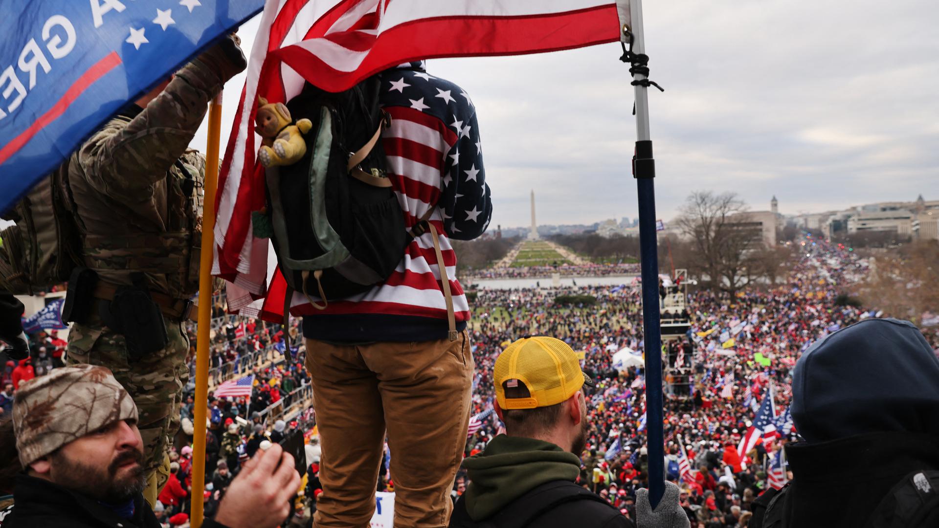 Demonstranten mit US-Flaggen stehen auf der Terrasse des Kapitols und überblicken den Vorplatz, auf dem sich eine Menschenmenge drängt.