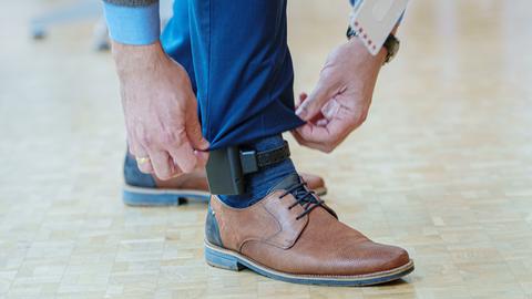 An einem Fuß ist oberhalb des Knöchels eine elektronische Fußfessel angebracht. 