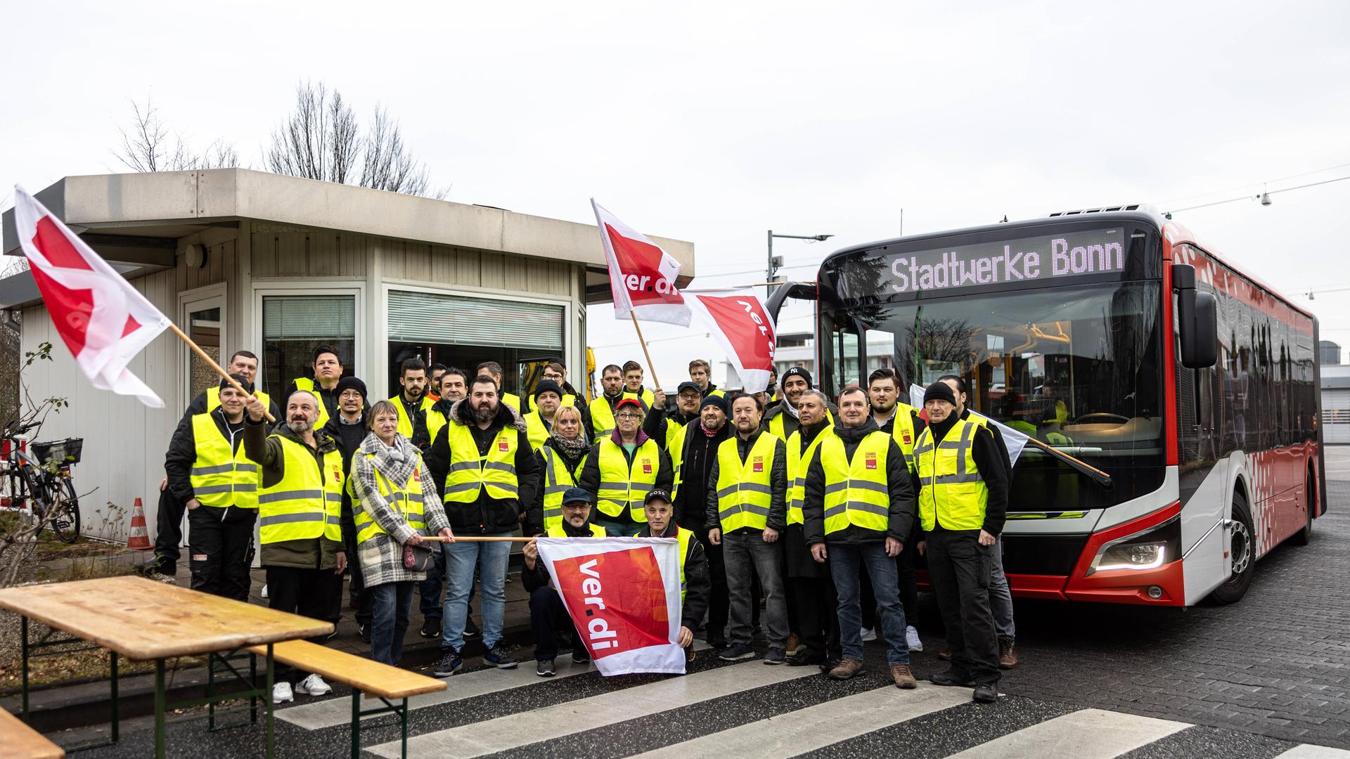 Streikende Mitarbeiter mit Fahnen und Bannern stehen vor einem Bus der Stadtwerke. Streikende Mitarbeiter mit Fahnen und Bannern stehen vor einem Bus der Stadtwerke.