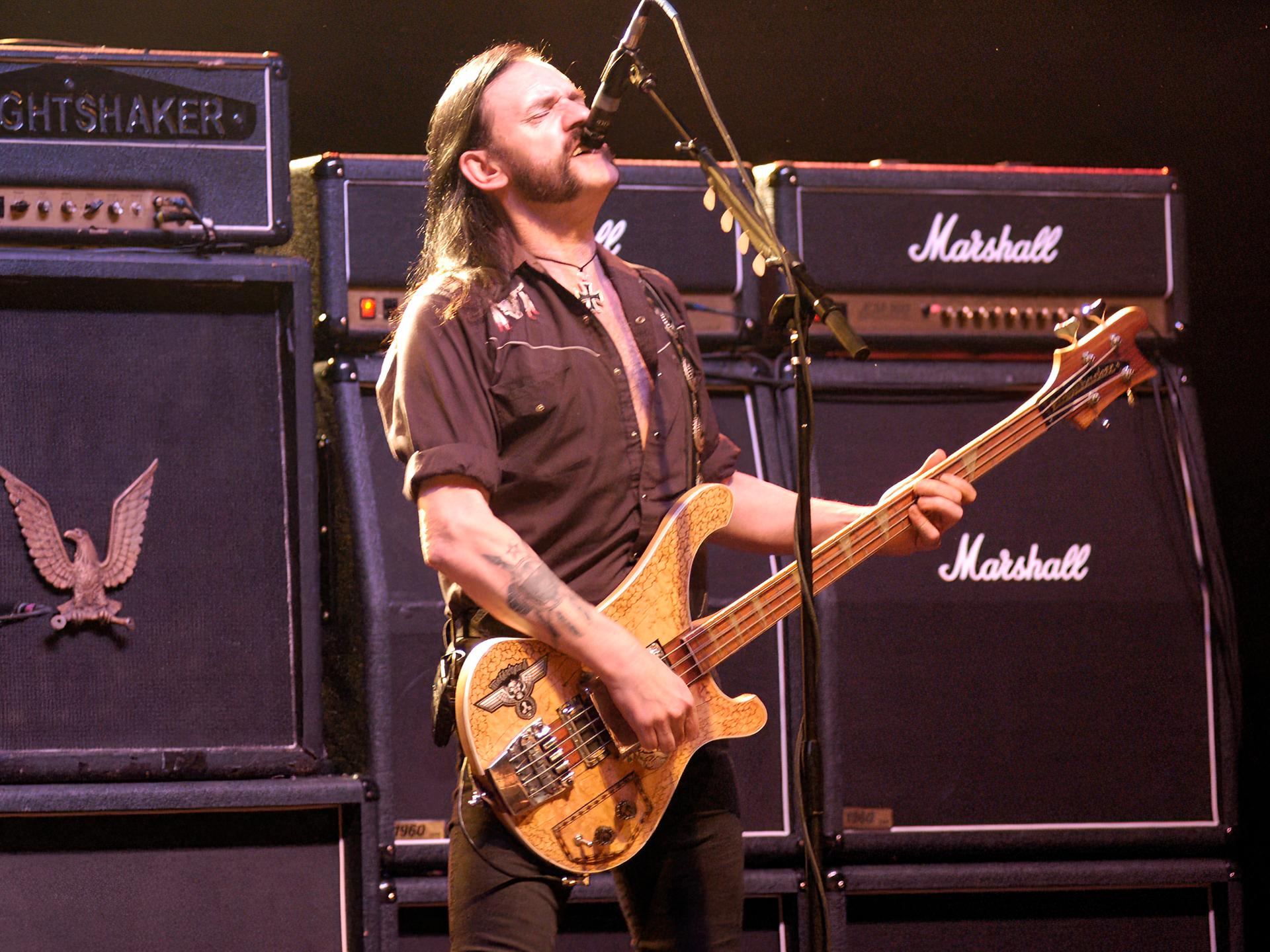 Der Motörhead-Frontman Lemmy Kilmister steht vor überdimensionierten Marshal-Verstärkern, brüllt in ein Mikrofon und spielt Bass