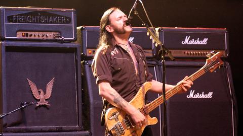 Der Motörhead-Frontman Lemmy Kilmister steht vor überdimensionierten Marshal-Verstärkern, brüllt in ein Mikrofon und spielt Bass