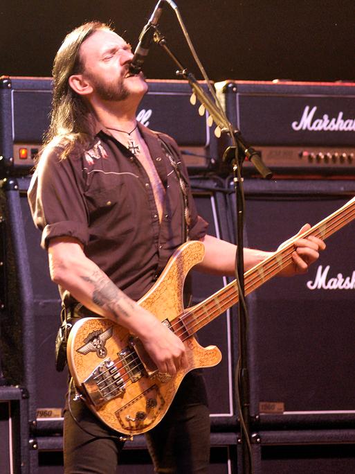 Der Motörhead-Frontman Lemmy Kilmister steht vor überdimensionierten Marshal-Verstärkern, brüllt in ein Mikrofon und spielt Bass