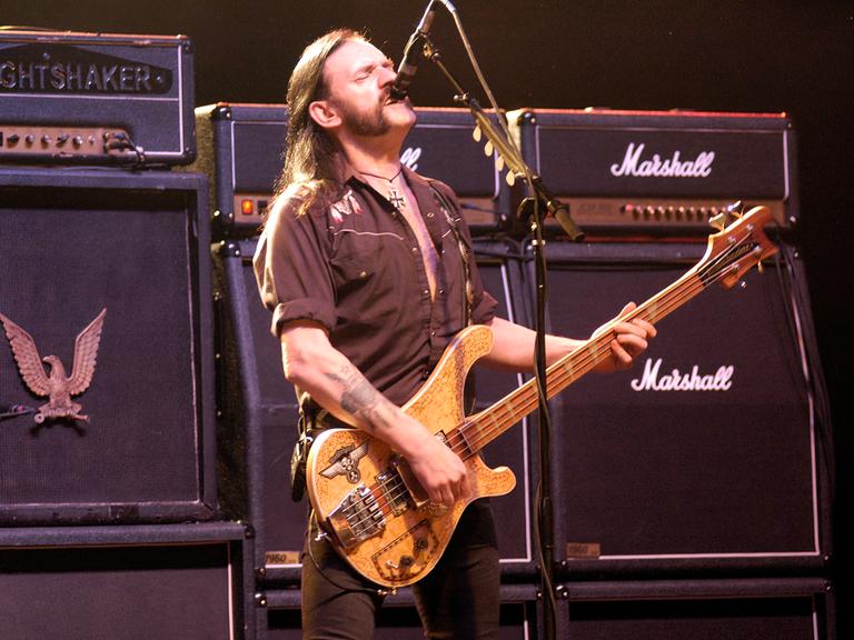 Der Motörhead-Frontman Lemmy Kilmister steht vor überdimensionierten Marshal-Verstärkern, brüllt in ein Mikrofon und spielt Bass