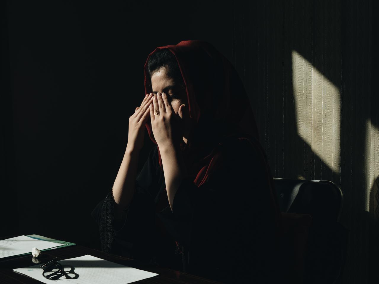 Eine afghanische Frau mit Kopftuch hält sich die Hände vor das Gesicht.