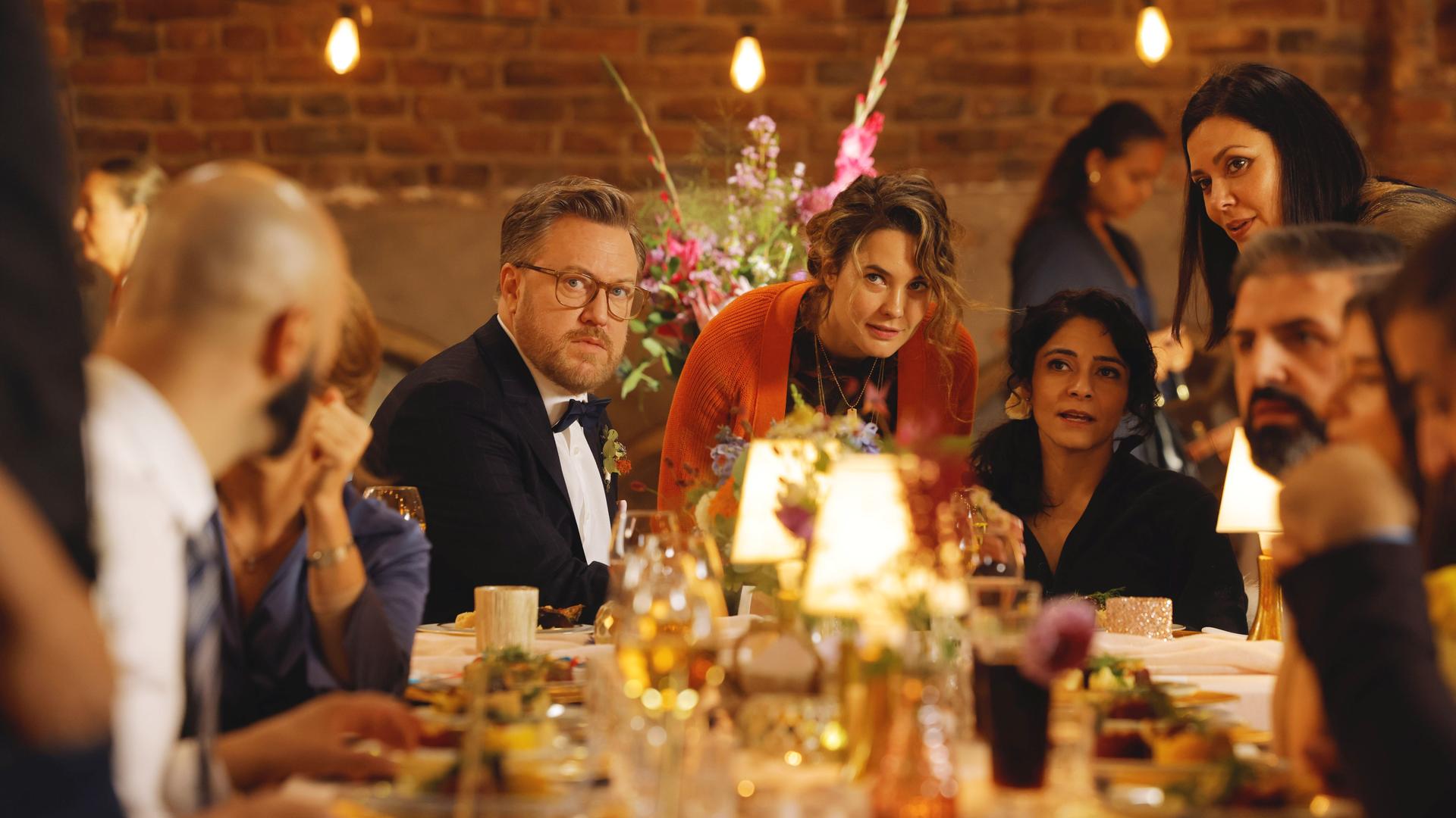 Filmszene aus Feste Freunde. Zu sehen sind Tom Trambow, Natalie (Jasmin Shakeri) und Maya (Katia Fellin) mit den Frischvermählten Rolf (Nicholas Ofczarek) und Dina (Pegah Ferydoni) an einer festlichen Tafel.