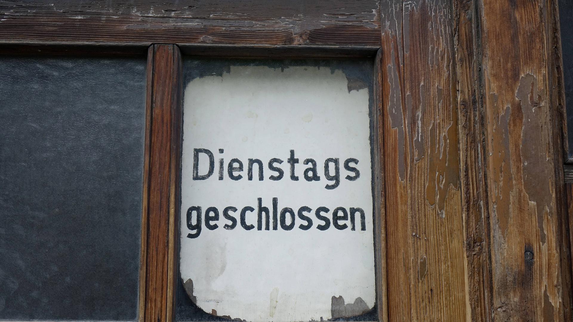 Ein altes weißes Schild, in einer alten Glastüre, auf dem steht: "Dienstags geschlossen"