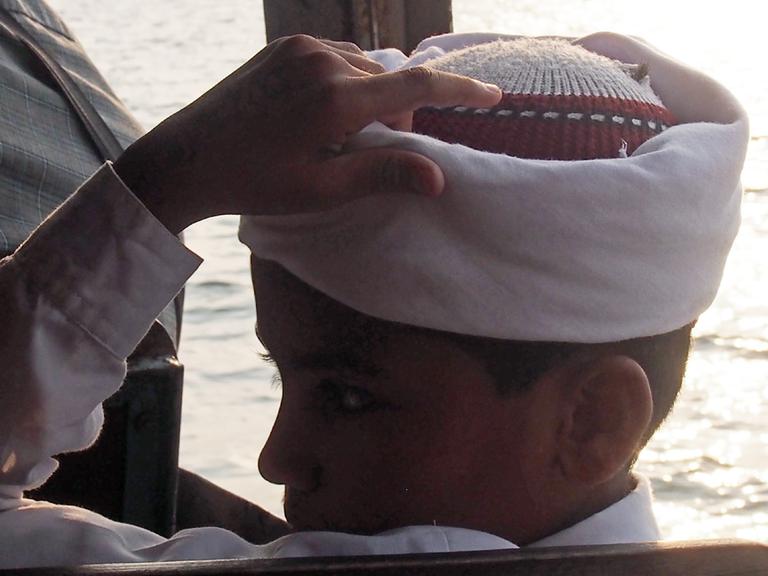 Im südindischen Kochi erlebt Aleš Šteger eine Überfülle an Farben, Aromen und den "Puls eines Lebens, das in einem Moment von der Tragödie zur Freude umschlägt". Zu sehen: Ein Junge im Profil sitzt auf einem Passagierboot und hält die linke Hand an seinem Kopf. 