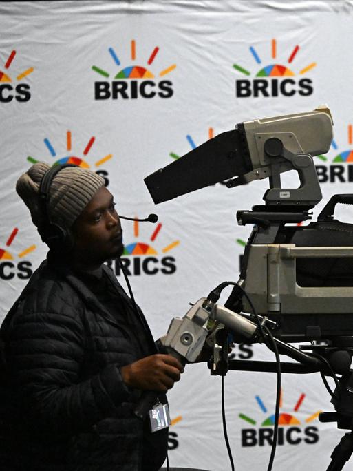 Ein Kameramann filmt beim 15. Gipfel der BRICS-Staaten in Südafrika vor einem Hintergrund mit "BRICS"-Logos. 