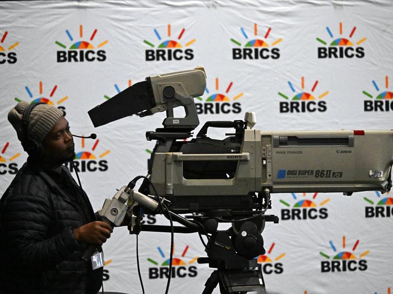 Ein Kameramann filmt beim 15. Gipfel der BRICS-Staaten in Südafrika vor einem Hintergrund mit "BRICS"-Logos. 